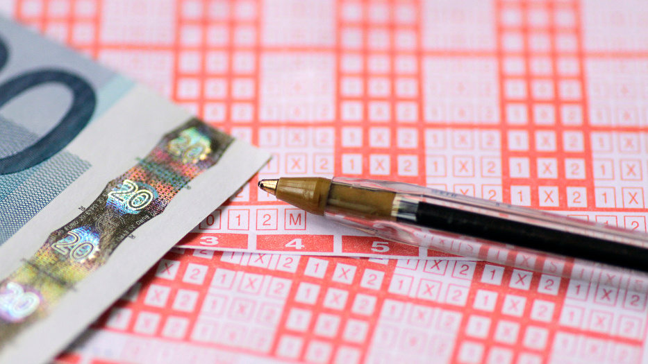 Zwei Lotto-Scheine mit rötlichem Muster. Auf den Scheinen liegt ein Kugelschreiber und ein 20-Euro-Schein. 